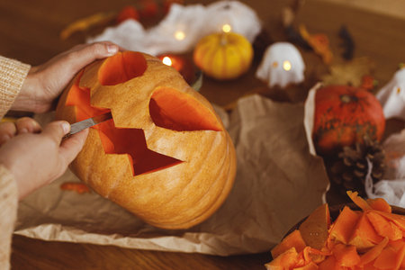 Carving halloween pumpkin. Woman holding pumpkin and knife on table with ghosts and spiders. Carve a jack o lantern, halloween preparation. Making halloween decorationsの写真素材