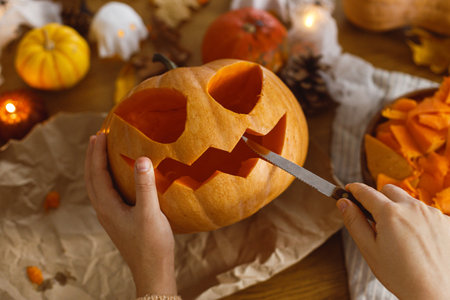 Happy Halloween! Carving halloween pumpkin. Woman holding pumpkin and knife on table with ghosts and spiders. Making halloween decorationsの写真素材