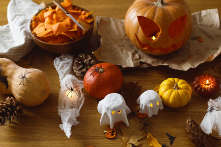 Happy Halloween! Carving Jack o lantern pumpkin, glowing ghosts and spiders on table in living room. Spooky atmospheric halloween decorationsの写真素材