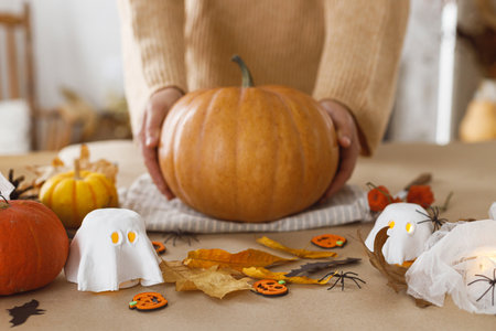Carving halloween pumpkin. Woman holding pumpkin on table with ghosts and spiders in living room. Carve a pumpkin, halloween preparation. Making halloween decorationsの写真素材