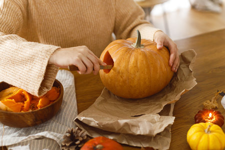 Carving halloween pumpkin. Woman holding pumpkin and gutting on table with ghosts and spiders in living room. Carve a pumpkin, halloween preparation. Making halloween decorationsの写真素材