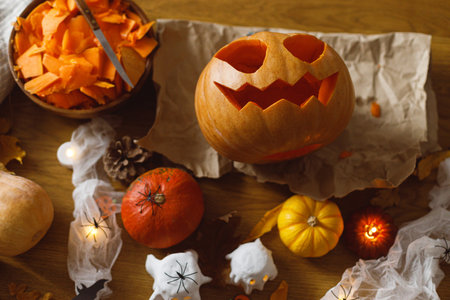 Happy Halloween! Carving Jack o lantern pumpkin, glowing ghosts and spiders on table in living room. Spooky atmospheric halloween decorationsの写真素材
