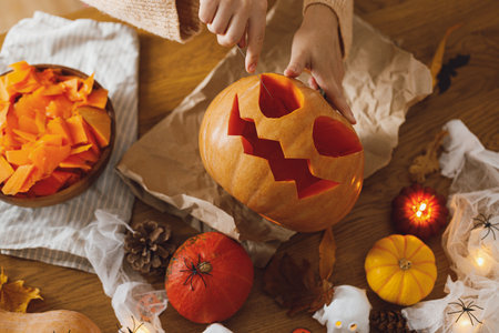 Making jack o lantern. Woman carving halloween pumpkin on table with ghosts and spiders, halloween preparation. Happy halloween! Making festive decorationsの写真素材