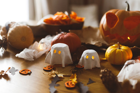 Happy Halloween! Carving Jack o lantern pumpkin, glowing ghosts and spiders on table in living room. Spooky atmospheric halloween decorationsの写真素材