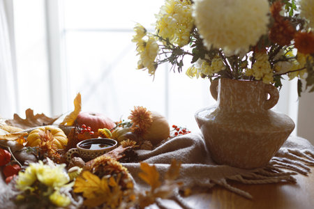Autumn cozy still life. Cup of tea, pumpkins, fall leaves and flowers in vase, berries and pine cones on table. Fall hygge, space for text. Thanksgiving backgroundの写真素材