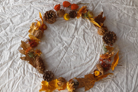 Autumn wreath flat lay. Autumn flowers, fall leaves, berries and pine cones on linen cloth top view. Happy Thanksgiving. Hello Fall background, space for text.の写真素材