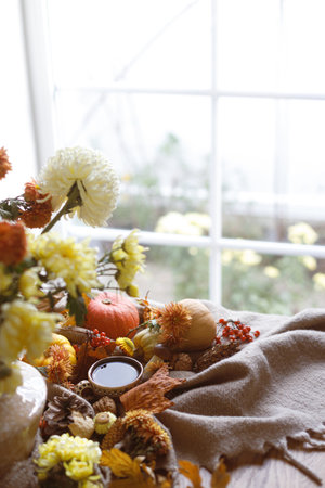 Autumn cozy still life. Cup of tea, pumpkins, fall leaves and flowers in vase, berries and pine cones on table. Fall hygge, space for text. Thanksgiving backgroundの写真素材