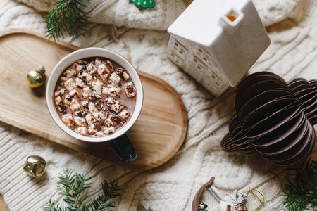 Christmas flat lay. Cup of hot chocolate with marshmallow, christmas ornaments, cozy knitted sweater and fir branches on background of stylish christmas tree with golden lights. Winter bannerの写真素材