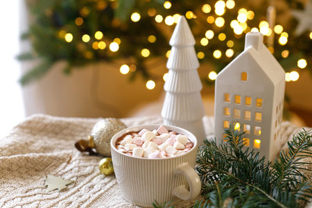 Christmas background. Cup of hot chocolate with marshmallows, christmas ornaments, cozy knitted sweater and fir branches against stylish tree with lights. Merry Christmas. Winter hyggeの写真素材