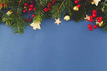 Christmas flat lay. Green fir branches, red berries and golden ornaments on blue background. Merry Christmas. Stylish christmas border with space for text. Xmas backgroundの写真素材