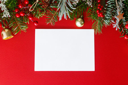 Christmas card mock up. Empty greeting card flat lay with fir branches, red berries and golden ornaments on red background. Merry Christmas. Season greetings templateの写真素材