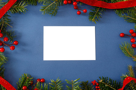 Christmas card flat lay. Modern greeting card mock up with fir branches, red berries on blue background. Empty postcard template, space for text. Merry Christmasの写真素材