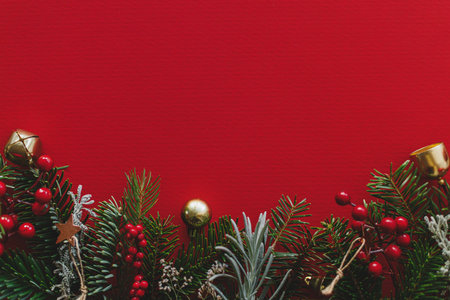 Christmas flat lay. Green fir branches, red berries and golden ornaments on red background. Merry Christmas. Stylish christmas border with space for text. Xmas backgroundの写真素材