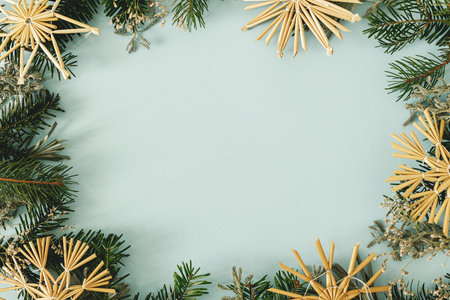 Stylish Christmas frame flat lay. Green fir branches and eco straw ornaments on light blue background. Modern christmas frame with space for text. Season's greeting cardの写真素材