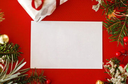 Christmas card flat lay. Modern greeting card mock up with fir branches, red berries and golden ornaments on red background. Empty postcard template, space for text. Merry Christmasの写真素材