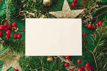 Christmas card mock up. Empty greeting card flat lay with fir branches, red berries and glitter ornaments on green background. Merry Christmas. Season greetings templateの写真素材