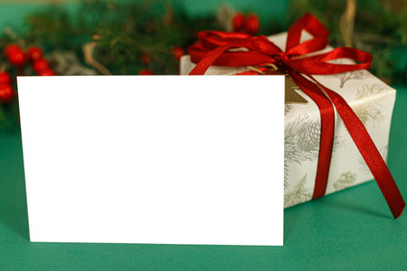 Christmas card mock up. Empty greeting card  with fir branches, red berries and gift box on green background. Merry Christmas. Season greeting postcard templateの写真素材