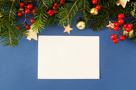 Christmas card mock up. Empty greeting card flat lay with fir branches, red berries and golden ornaments on blue background. Merry Christmas. Season greetings templateの写真素材