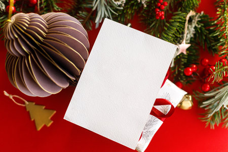 Empty greeting card and fir branches, red berries, gold ornaments on red background top view. Christmas card mockup with space for text.  Xmas Postcard. Season greetings card templateの写真素材