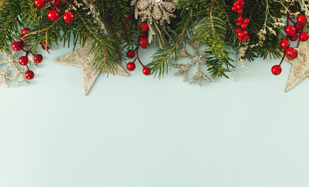 Christmas flat lay. Green fir branches, red berries and glitter ornaments on light blue background. Merry Christmas. Stylish christmas border with space for text. Xmas backgroundの写真素材