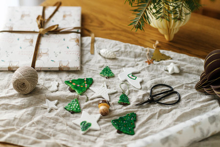 Wrapping christmas gift. Modern authentic Christmas ornaments. Stylish handmade clay tree, star and mushrooms with scissors and thread on rustic table. Winter holiday preparationの写真素材