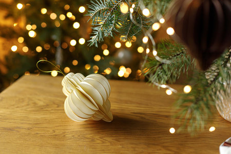 Modern Christmas ornament. Stylish paper decoration on wooden table against christmas tree with golden lights bokeh. Winter holiday preparation.の写真素材