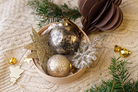 Decorating christmas tree with vintage golden baubles. Stylish Christmas ornaments in box on knitted blanket with fir branches. Winter holiday preparation aesthetic. Merry Christmasの写真素材