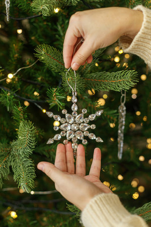Decorating christmas tree with vintage ornaments. Hands in cozy sweater hanging stylish Christmas star on christmas tree with golden lights. Merry Christmasの写真素材