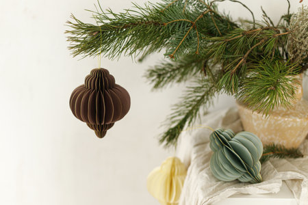 Stylish christmas paper ornaments on spruce branches in vase. Modern rustic winter bouquet on table in scandinavian room. Christmas home authentic decorの写真素材