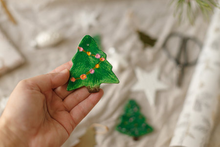 Christmas ornaments. Hand holding stylish handmade clay tree on background of ribbons and decorations on modern wrapping paper. Christmas gift decor. Winter handicraftsの写真素材
