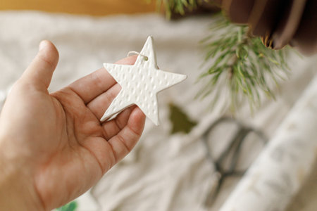 Christmas ornaments. Hand holding stylish handmade clay star on background of scissors and decorations on table. Christmas gift decor. Winter handicraftsの写真素材