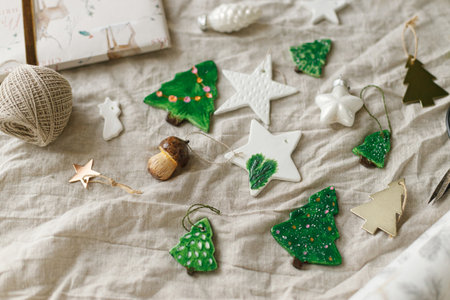 Modern authentic Christmas ornaments. Stylish handmade clay tree,star and mushrooms with scissors and thread on rustic table. Christmas gift decor. Winter handcraft and holiday preparationの写真素材