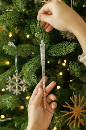 Decorating christmas tree with vintage ornaments. Hands in cozy sweater hanging stylish Christmas ornaments on christmas tree with golden lights. Merry Christmasの写真素材
