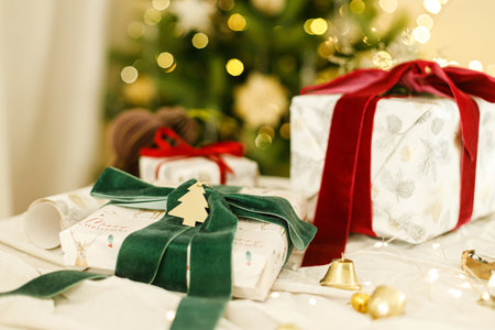 Stylish christmas gifts with spruce branch and modern ornaments on background of decorated christmas tree with golden lights. Merry Christmas and Happy Holidays. Modern Christmas presentの写真素材