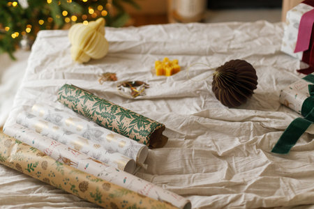 Wrapping stylish christmas gift, winter holidays preparation. Modern wrapping paper, ribbons and stylish ornaments on table with linen cloth. Details of festive decorationsの写真素材