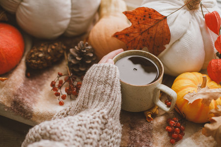 Hand in warm sweater holding warm cup of tea and pumpkins, fall leaves and candle on window sill. Autumn hygge, ugc concept. Happy Thanksgivingの写真素材