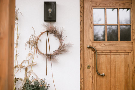 Modern fall decor of farm house entrance. Rustic wreath, pumpkins, moms flowers, corn at front door. Thanksgiving and Halloween. Rural autumn decorationの写真素材