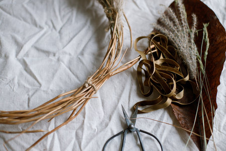 Dried grass, herbs, leaves, ribbon and scissors on rustic table. Details of making stylish autumn wreath. Fall decor and arrangement in home. Thanksgiving and Halloweenの写真素材