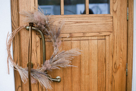Front door with stylish autumn wreath. Rustic wreath with dried grass, herbs and ribbon. Fall decor of house entrance. Thanksgiving and Halloweenの写真素材