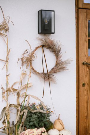 Modern fall decor of farm house entrance. Rustic wreath, pumpkins, moms flowers, corn at front door. Thanksgiving and Halloween. Rural autumn decorationの写真素材