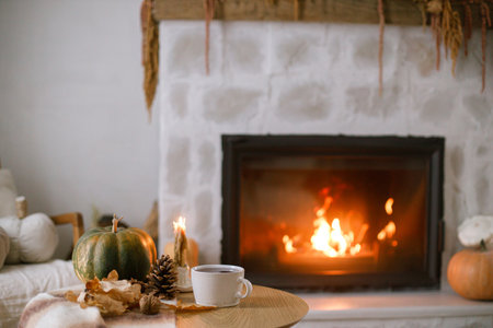 Cozy autumn. Cup of tea, pumpkin, autumn leaves on wooden table on background of warm fireplace. Fall still life in living room. Thanksgiving and Halloween.の写真素材