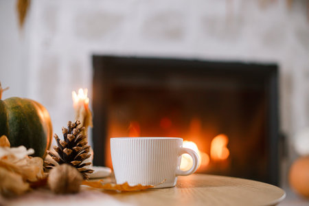 Cozy autumn. Cup of tea, pumpkin, autumn leaves on wooden table on background of warm fireplace. Fall still life in living room. Thanksgiving and Halloween.の写真素材