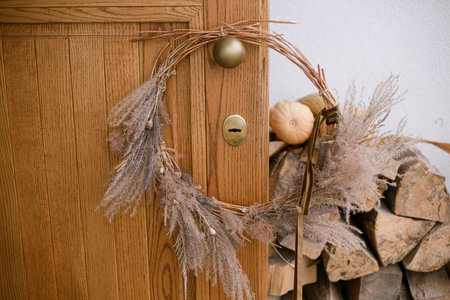 Stylish modern autumn wreath on wooden doors. Fall decor of farm house entrance. Rustic wreath with dried grass, herbs and ribbon. Thanksgiving and Halloweenの写真素材