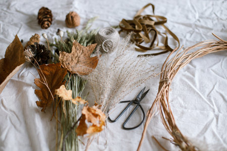 Dried grass, herbs, leaves, ribbon and scissors on rustic table. Details of making stylish autumn wreath. Fall decor and arrangement in home. Thanksgiving and Halloweenの写真素材