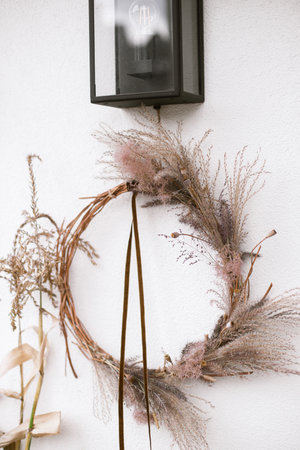Stylish autumn wreath at wooden doors. Fall decor of farm house entrance. Rustic wreath with dried grass, herbs and ribbon. Thanksgiving and Halloweenの写真素材