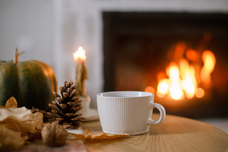 Warm cup of tea, pumpkin, autumn leaves on wooden table on background of burning fireplace. Cozy autumn still life. Thanksgiving and Halloween. Fall hyggeの写真素材