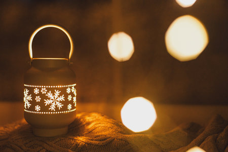 Merry Christmas! Stylish glowing christmas lantern and golden lights bokeh on cozy sweater at snowy window in night. Atmospheric magical scene. Christmas holiday banner. Space for textの写真素材