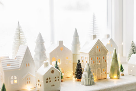 Christmas little ceramic houses, white snowy trees and golden lights on window. Xmas background. Merry Christmas! Atmospheric Christmas scene, miniature holiday villageの写真素材