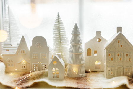 Merry Christmas! Stylish Christmas miniature holiday village with glowing golden lights on cozy blanket at snowy window. Atmospheric magical scene. Christmas holiday banner.の写真素材