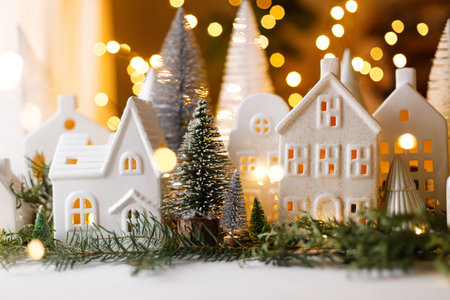 Merry Christmas! Stylish Christmas miniature holiday village with houses, trees, fir branches on background of golden lights bokeh in evening. Atmospheric magical scene. Holiday bannerの写真素材